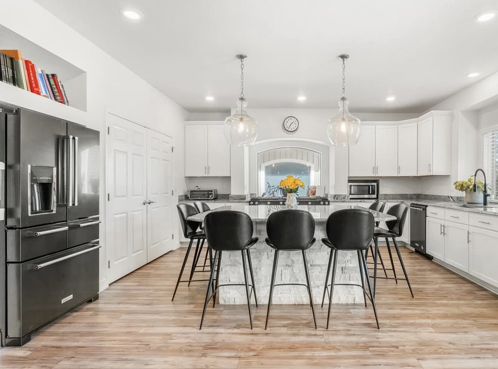 White kitchen with stone island, glass pendants and black bar stools in Aurora, CO