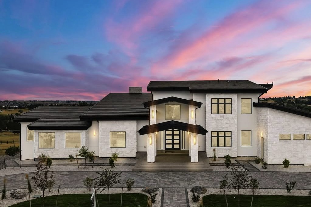 Twilight exterior of a white stone luxury home under a pink sunset sky