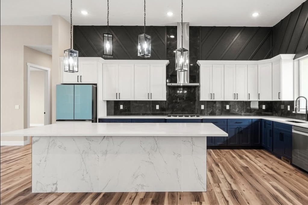 Kitchen with a black accent wall, navy lower cabinets and a marble island